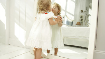 Baby girl (18-24 months) looking in mirror, hands pressed on glass