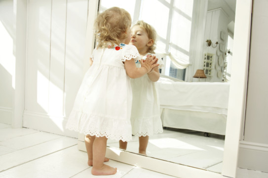 Baby girl (18-24 months) looking in mirror, hands pressed on glass