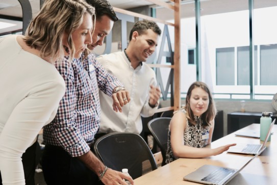 Group of office workers looking at a laptop screen.