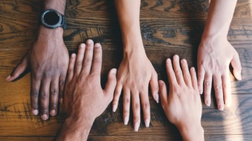 A group of hands laid out on a table together.