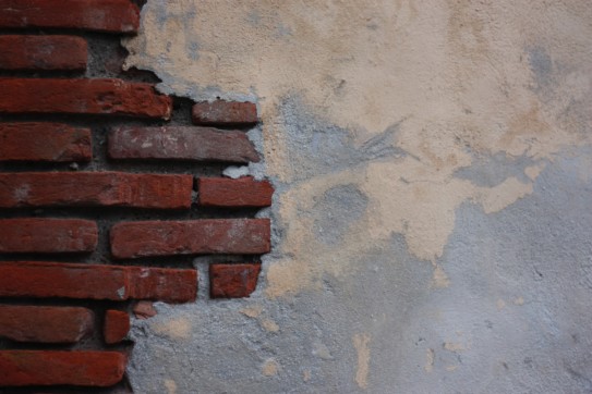 Brick wall half-covered in plaster.