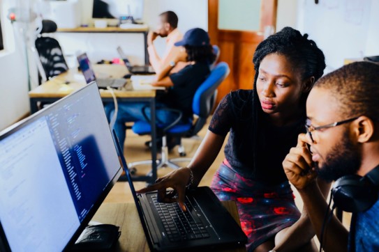 A woman overlooking a man using a computer.