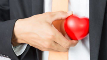 Businessman holds out the red heart, isolated background