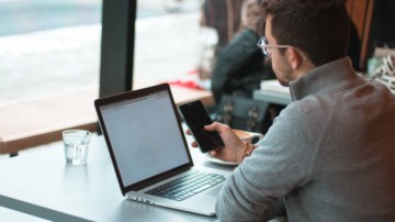 Man checking on his smartphone with his laptop open.