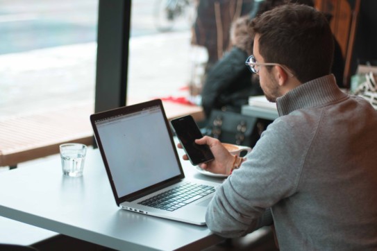 Man checking on his smartphone with his laptop open.