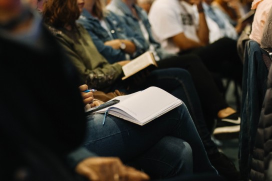 Closeup of an audience member taking notes.