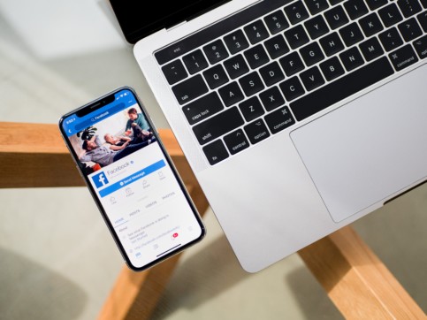 Facebook app on a smartphone next to a laptop.