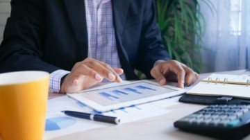 Closeup of a man's hand on a tablet displaying bar charts.